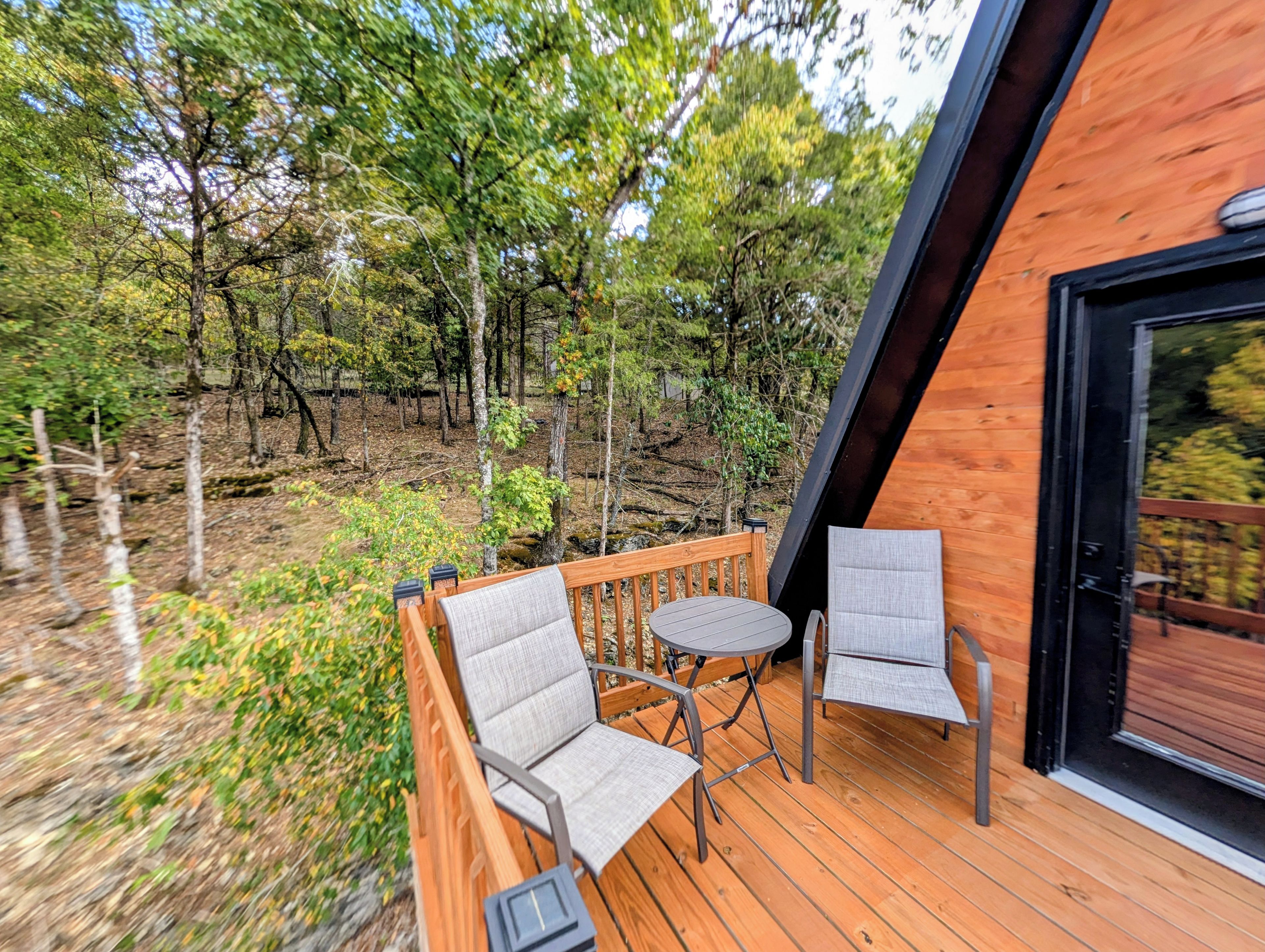 An outdoor deck with two chairs and a table, surrounded by trees.