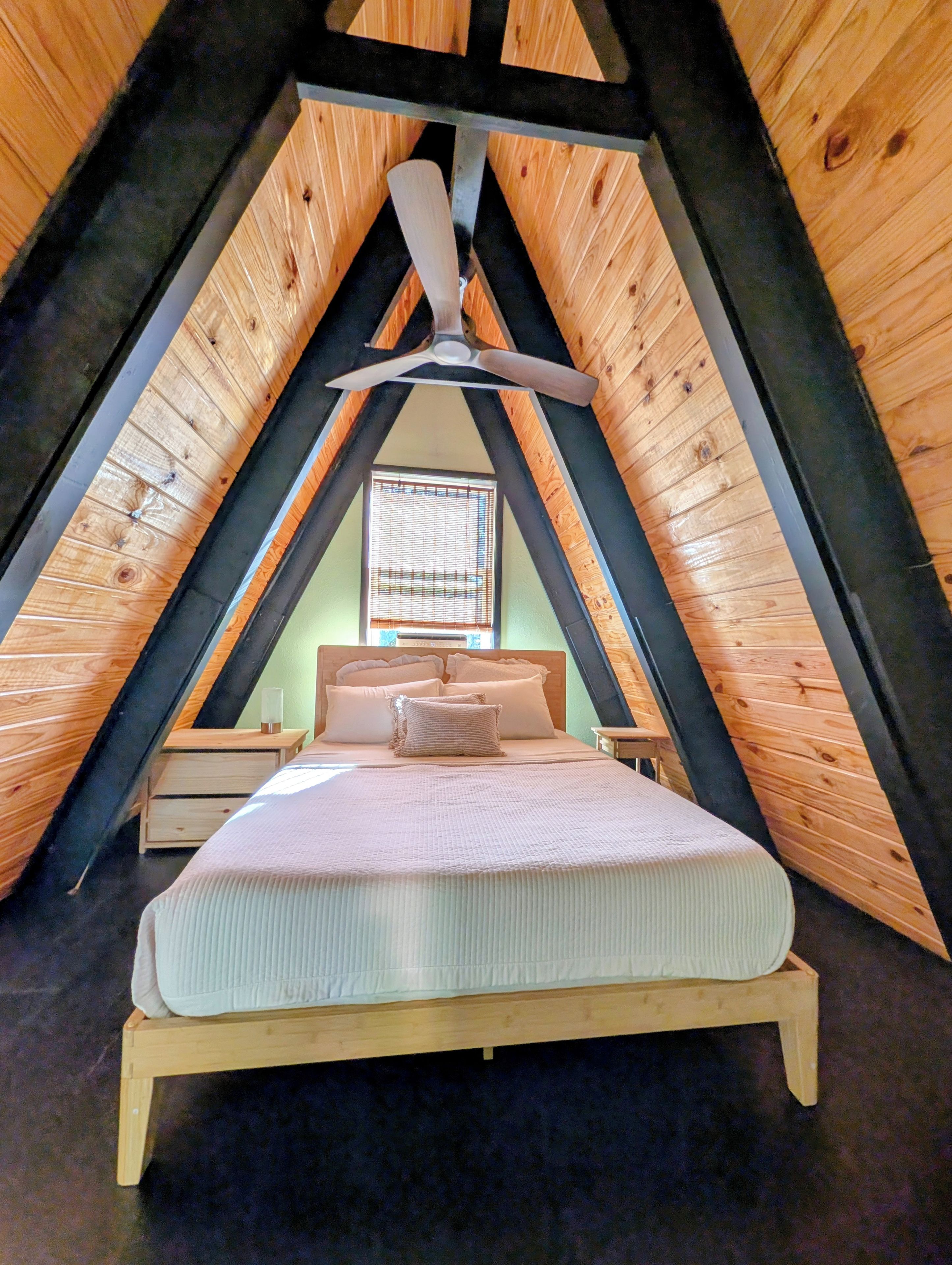 A bedroom with a sloped ceiling, a bed, a nightstand, and a ceiling fan.