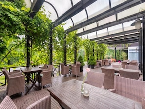 Eine Terrasse im Freien mit Korbmöbeln und einer Glaskuppel, umgeben von viel Grün.