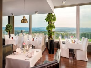 Ein Restaurant mit gedeckten Tischen, großen Fenstern mit Blick auf die Landschaft und einer Hängeleuchte.