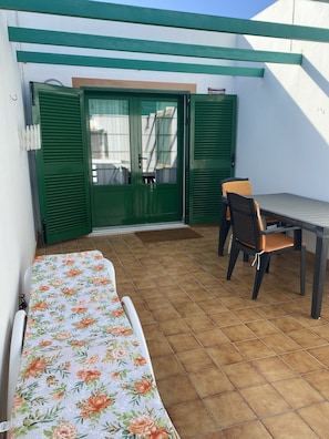 Une petite terrasse avec une table et des chaises, un banc abrité et une porte verte.