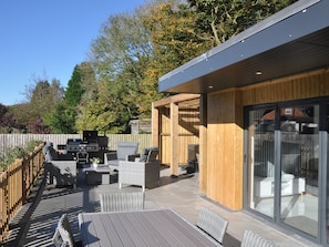 Eine moderne Terrassenanlage im Freien mit integriertem Grill, Korbmöbeln und einem Holzboden.
