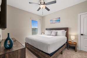 A bedroom with a bed, a ceiling fan, a window with blinds, a painting, a bedside table with a lamp, and a door. - NEW   Family Reunion Epic Game Room   Resort Pool 7837 (Kissimmee)