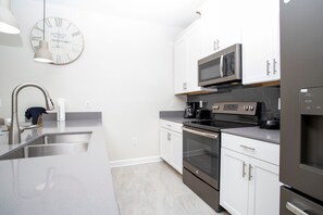 A modern kitchen with stainless steel appliances, white cabinetry, and a vintage clock on the wall. - NEW 5BR Private Pool  Lazy River   Resort 8955 (Kissimmee)