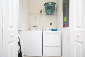 Een wasruimte met twee witte wasmachines, een groene wasmand op een plank en een brandveiligheidssymbool aan de muur.