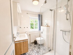 Ein modernes Badezimmer mit Duschkabine aus Glas, Waschbecken in Weiß und Toilette.