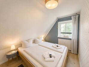 Ein Schlafzimmer mit zwei Betten, einem Nachttisch, einer Lampe, einem Fenster mit Vorhängen und einer Heizung.