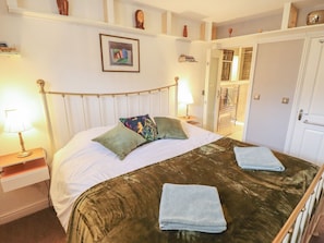 A neatly made bed with a green bedspread and two folded towels, a bedside lamp, and a framed picture on the wall. - Apartment 173 (Lincoln)