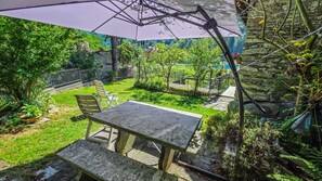 Eine Terrasse mit Tisch und Stühlen, umgeben von Grünpflanzen und einer Steinmauer.