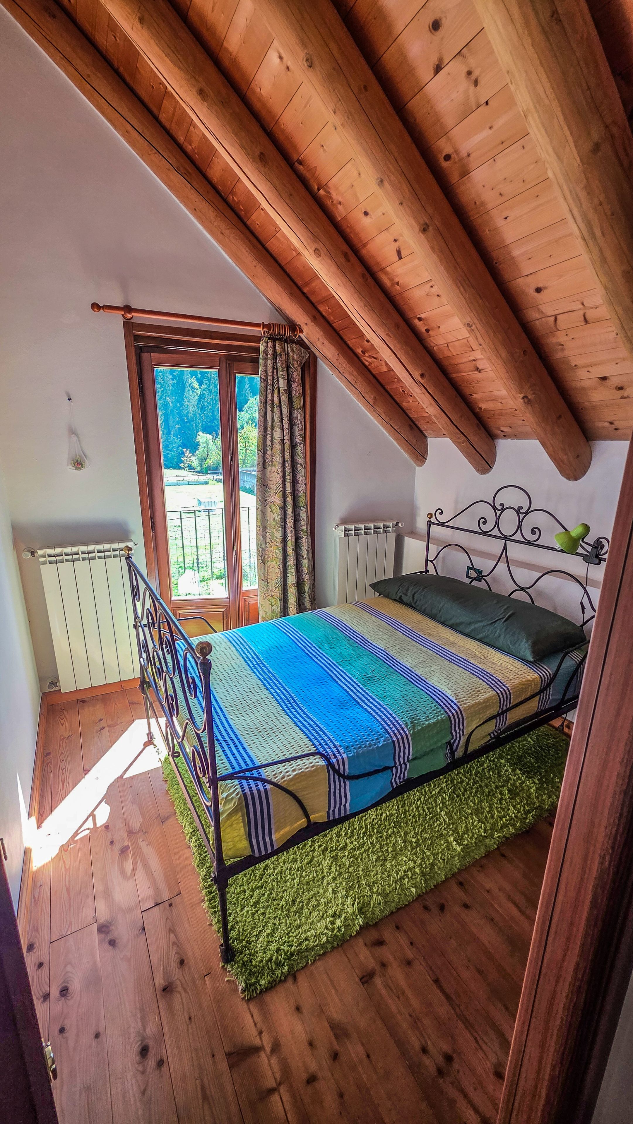 Una camera da letto con un letto, una finestra con tende, un termosifone e un soffitto in legno.