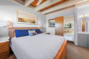 Ein Schlafzimmer mit einem Bett, Nachttischlampen, einem Gemälde und Blick auf einen Außenbereich.