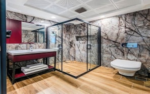 A modern bathroom with a glass-enclosed shower, a marble wall, and a wooden floor. - Heaven Prime Airport Hotel (Arnavutkoy, Turkiye)