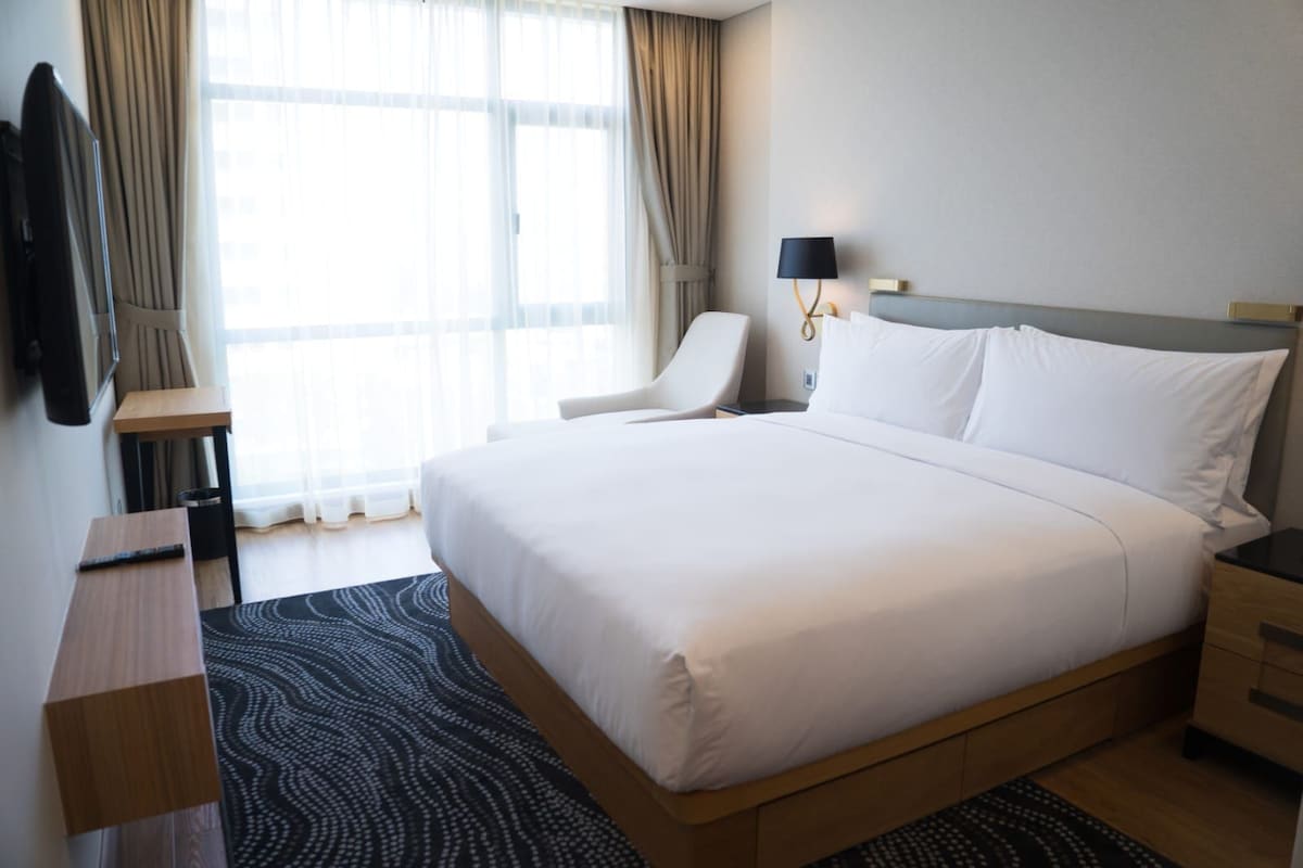 A hotel room with a large bed, a desk, a chair, and a lamp.