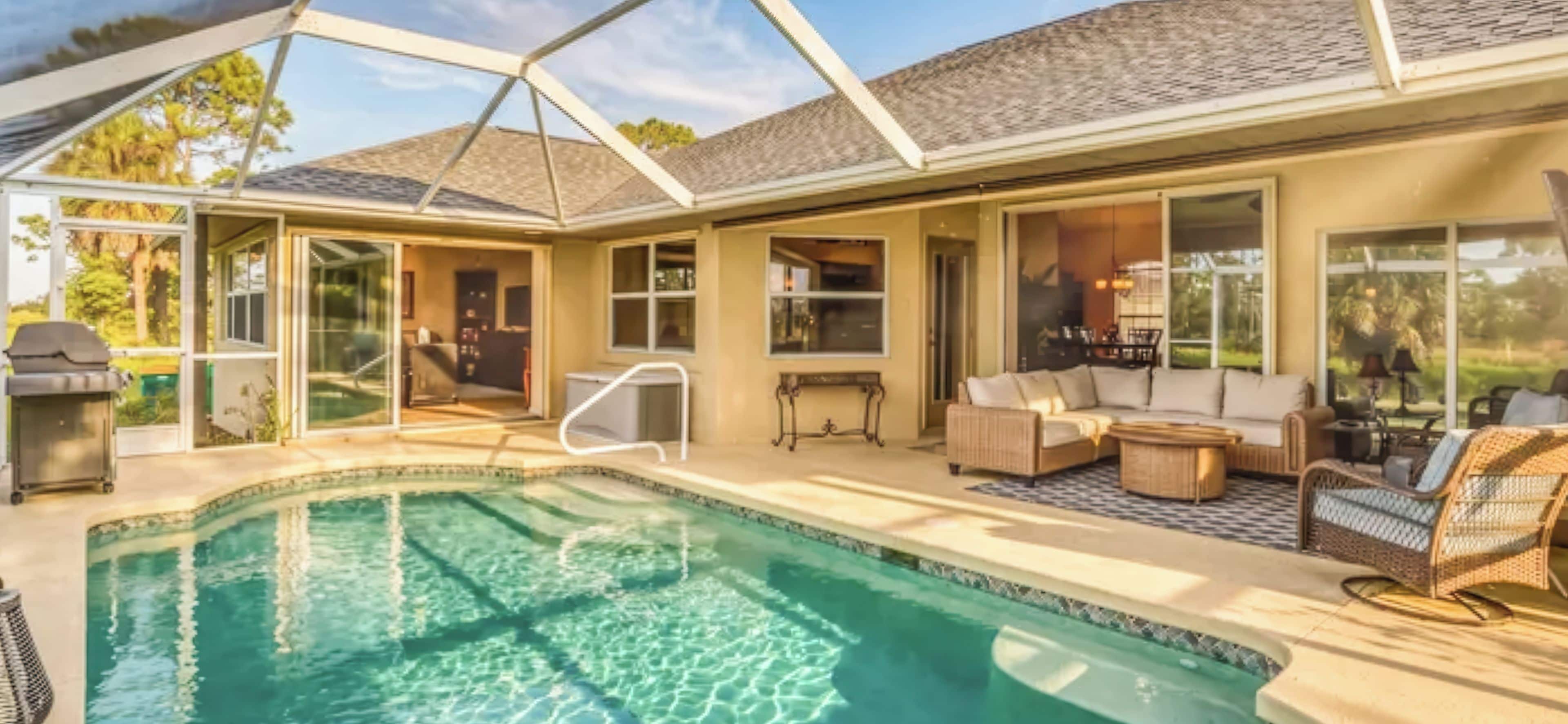 A poolside area with a clear pool, outdoor furniture, and a covered patio.