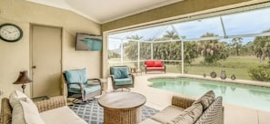 A poolside area with wicker furniture, a red chair, and a view of the outdoors. - Paradise Preserve (Rotonda West)