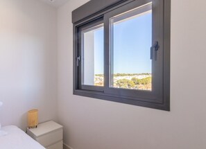 A bedroom with a window, a bedside table, and a lamp. - Alma Rosa - modern appartement met 80 m2 prive dakterras (Torrevieja)