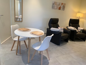 Uma sala de estar moderna com uma mesa de jantar redonda, duas cadeiras brancas, um sofá preto e um abajur.