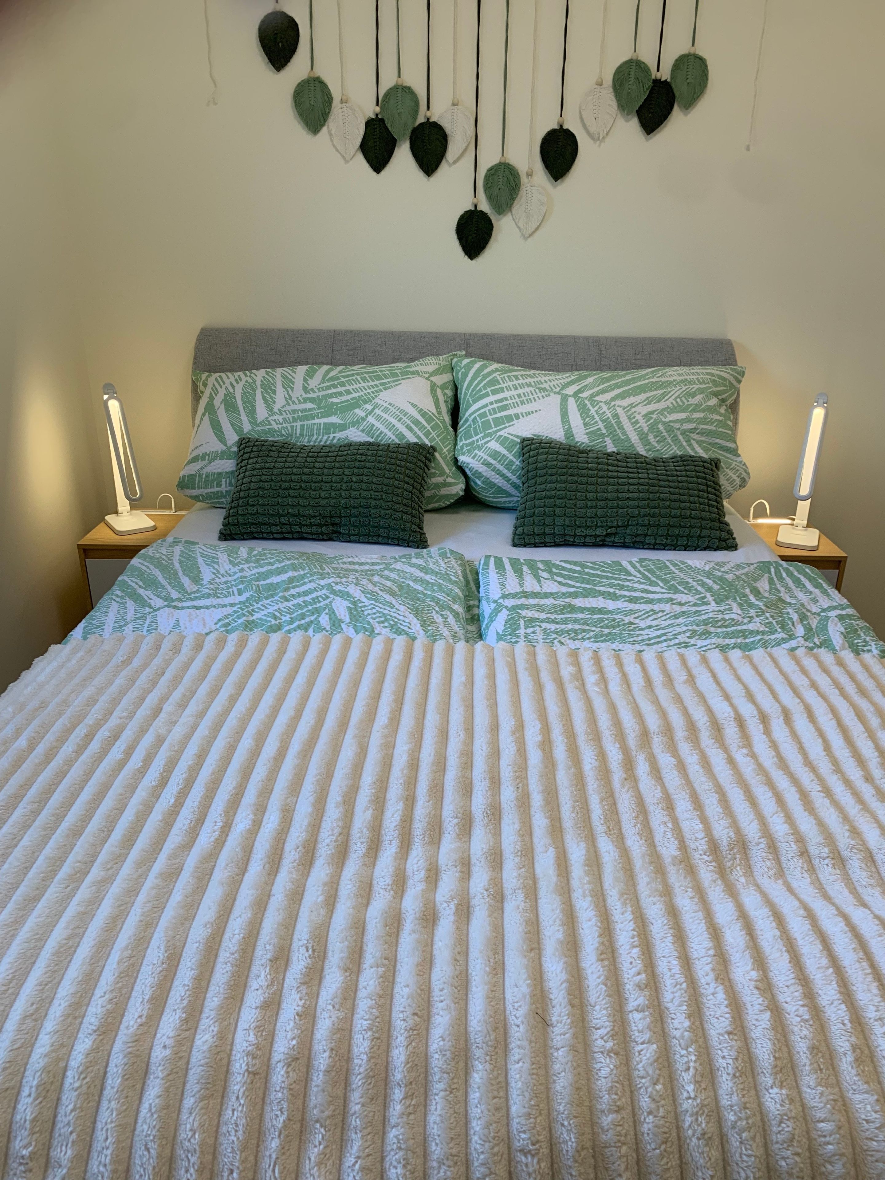 Uma cama com manta listrada, duas almofadas com padrão de folha e decoração de folhas penduradas na parede.