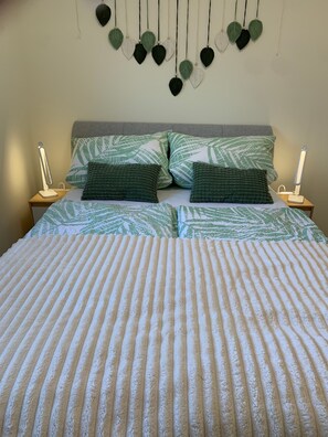 Uma cama com manta listrada, duas almofadas com padrão de folha e decoração de folhas penduradas na parede.