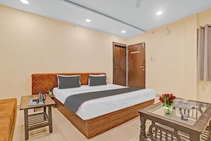 A hotel room with a bed, bedside table, and a small table with a vase of flowers. - Hotel O Uday Vilas (Indore)