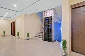 A hotel lobby with a modern elevator, a staircase, and potted plants. - Hotel O Uday Vilas (Indore)