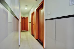 Un pasillo con puertas de madera, paredes de azulejos blancos y suelo de baldosas.