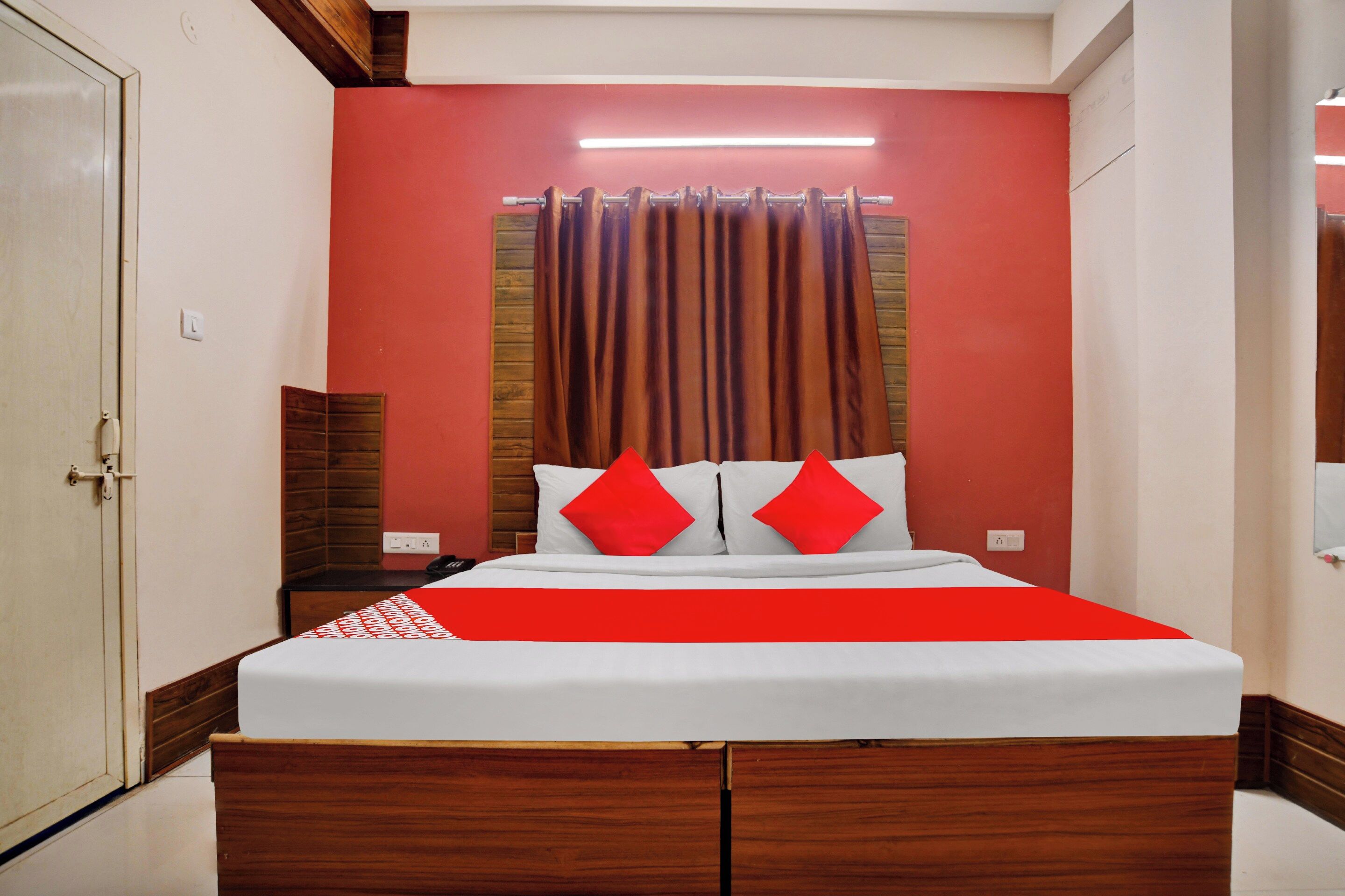 Una habitación de hotel con una cama, cabecera de madera, pared roja y puerta blanca.