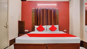 Una habitación de hotel con una cama, cabecera de madera, pared roja y puerta blanca.