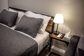 Een hotelkamer met een bed, kussens, een nachtkastje met een lamp, een telefoon en een prullenbak.