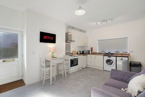 A compact living space with a kitchenette, a dining area, a washing machine, and a television displaying the Netflix logo. - Chic 1BR Stay near Darlington | Sleeps 2 | TV+WiFi (Darlington)