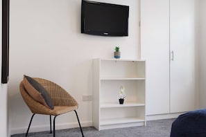 A room with a white wardrobe, a white shelving unit with a small plant, a wicker chair, and a black TV mounted on the wall. - Chic 1BR Stay near Darlington | Sleeps 2 | TV+WiFi (Darlington)