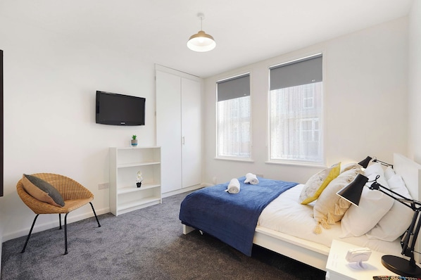 Ein modernes Hotelzimmer mit Bett, Sessel, Fernseher und Schreibtisch mit Lampe.