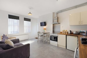 Ein kompakter Wohnraum mit Küchenzeile, Sofa, Esstisch und an der Wand befestigtem Fernseher.