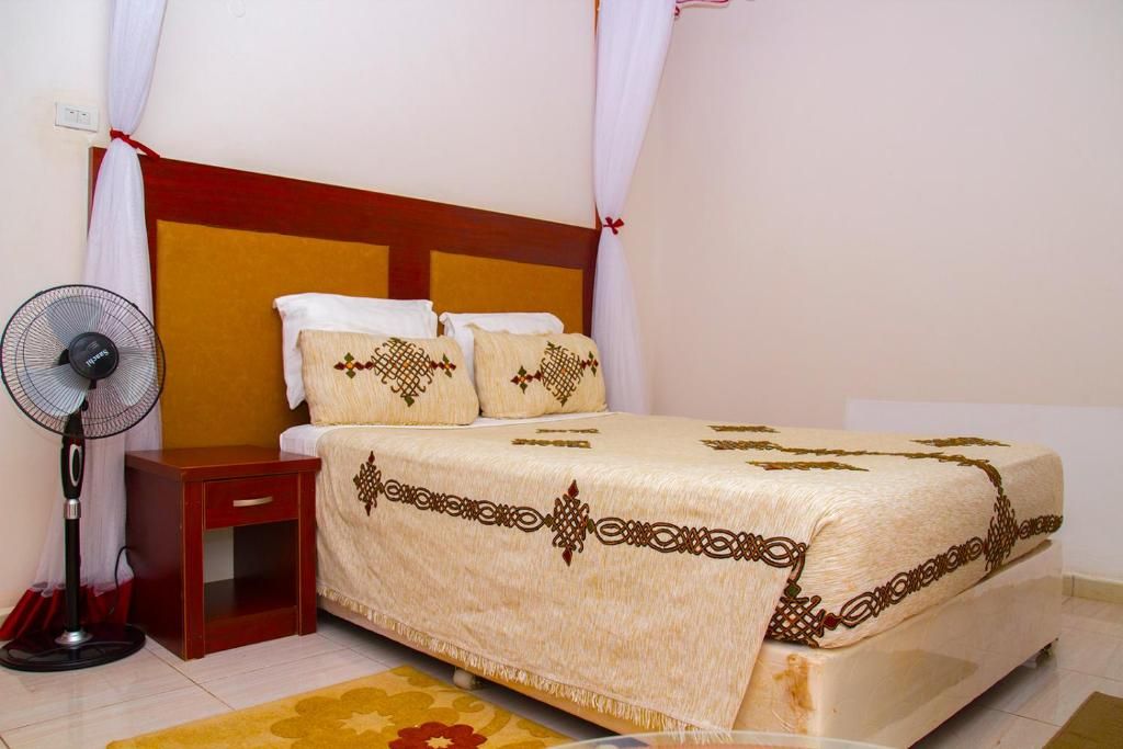 A bedroom with a bed, a bedside table, a fan, and a curtain.