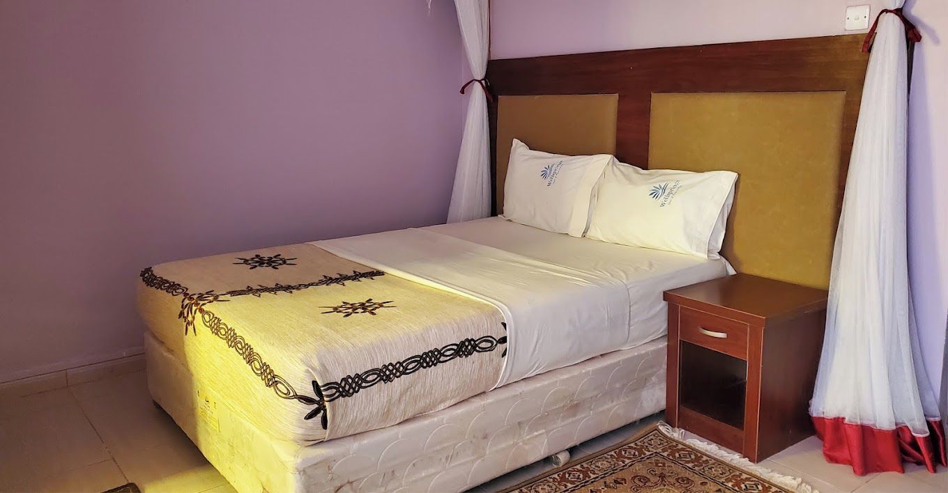 Una cama con cabecera, una mesita de noche y una alfombra estampada.
