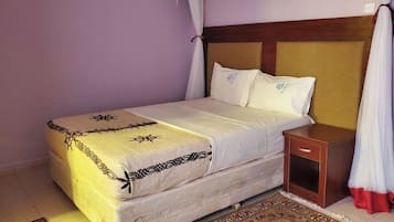 Una cama con cabecera, una mesita de noche y una alfombra estampada.