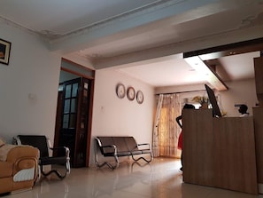 Una sala de estar con sofá, banqueta, aparador de madera y una puerta que da a otra habitación.