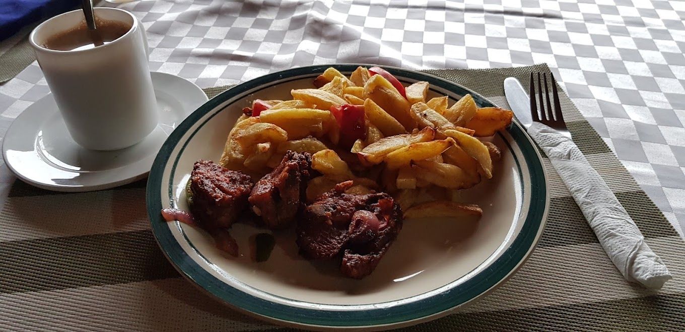 Un plato de comida con papas fritas, una taza de café y un tenedor sobre una mesa.