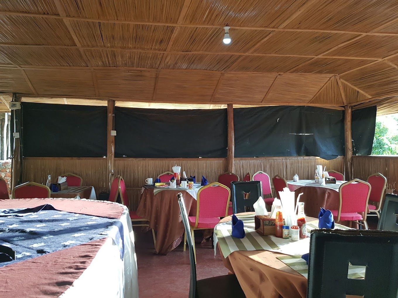 An indoor dining area with tables and chairs, covered by a roof.