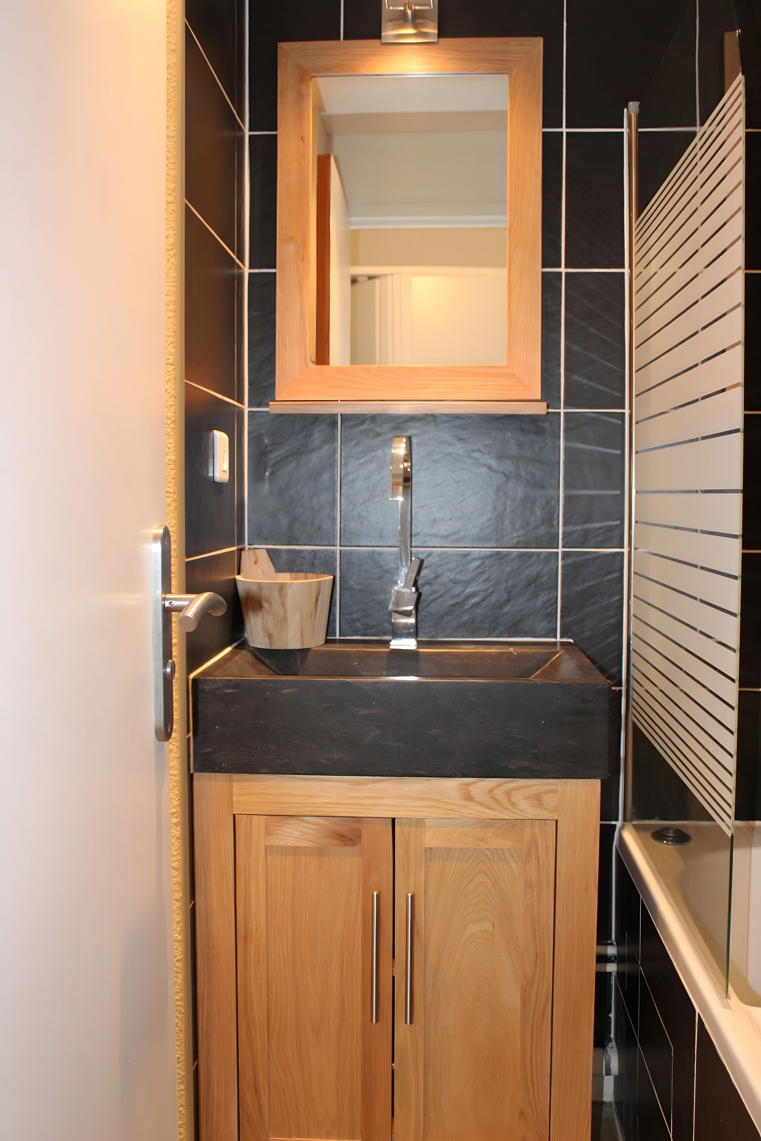 Une salle de bain moderne avec un meuble-lavabo en bois, un plan de toilette noir et un miroir au-dessus du lavabo.