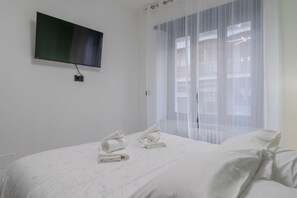 A hotel room with a bed, a TV mounted on the wall, and a window with sheer curtains. - Maison Tresor by Wonderful Italy (Turin)