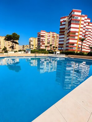 A swimming pool with reflections of buildings, surrounded by a paved area and greenery. - Apartment 'La Canoa 79' with Sea Views, Wi-Fi and Air Conditioning (Torrox)