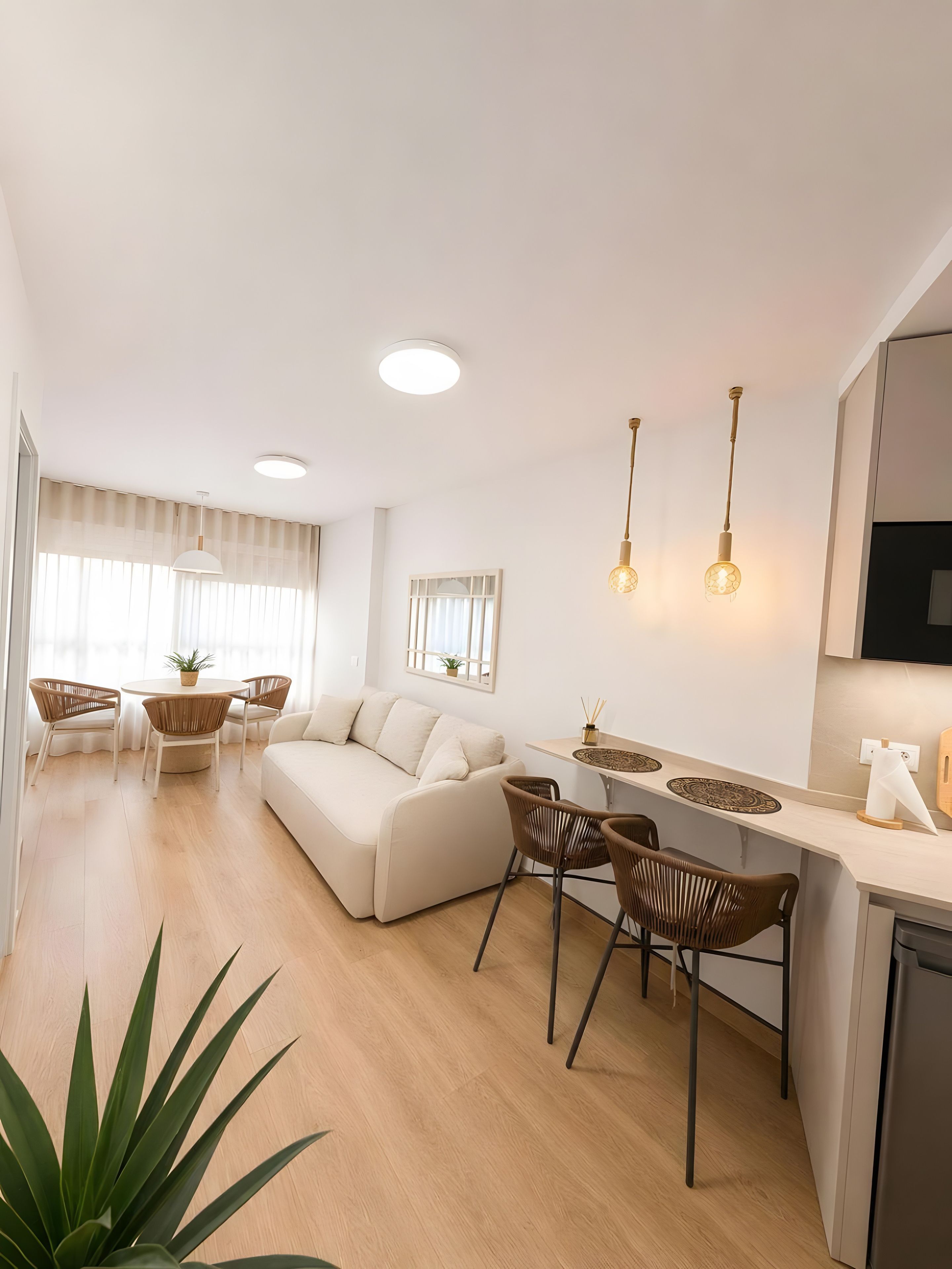 En moderne stue med sofa, spisebord, stole og et køkken med køleskab.