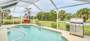 A pool area with a covered patio, a grill, and a red chair. - Paradise Preserve - Single-story 3-bedroom home with a pool and screened lanai in Rotonda West (Rotonda West)
