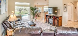 A spacious living room with a leather sofa set, a television, and a dining area with chairs. - Paradise Preserve - 3-Bedroom Bungalow with Pool and Enclosed Porch in Rotonda West (Rotonda West)