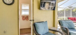 Ein Zimmer mit Korbmöbeln, einem an der Wand befestigten Fernseher und einem Fenster mit Blick ins Freie.