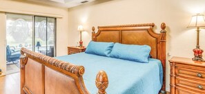 Ein Schlafzimmer mit einem hölzernen Bett, einer Glastür, die nach draußen führt, und einem Nachttisch mit einer Lampe.