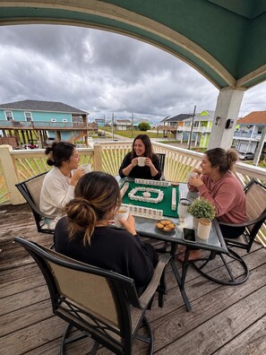 Eine Gruppe von Menschen spielt Mahjong auf einer Holzterrasse mit Blick auf Häuser im Hintergrund.