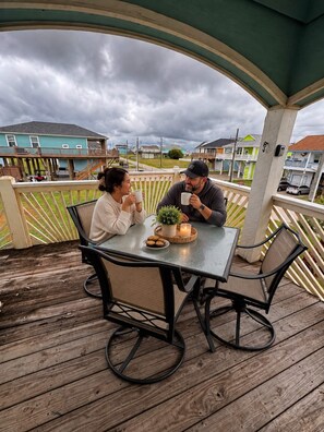 A covered outdoor seating area with a table and chairs, a potted plant, and a candle on the table. - Our house is not fancy; it is welcoming. (Bolivar Peninsula)