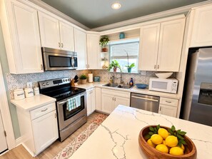 Cocina moderna con muebles blancos, electrodomésticos de acero inoxidable y encimera de mármol.